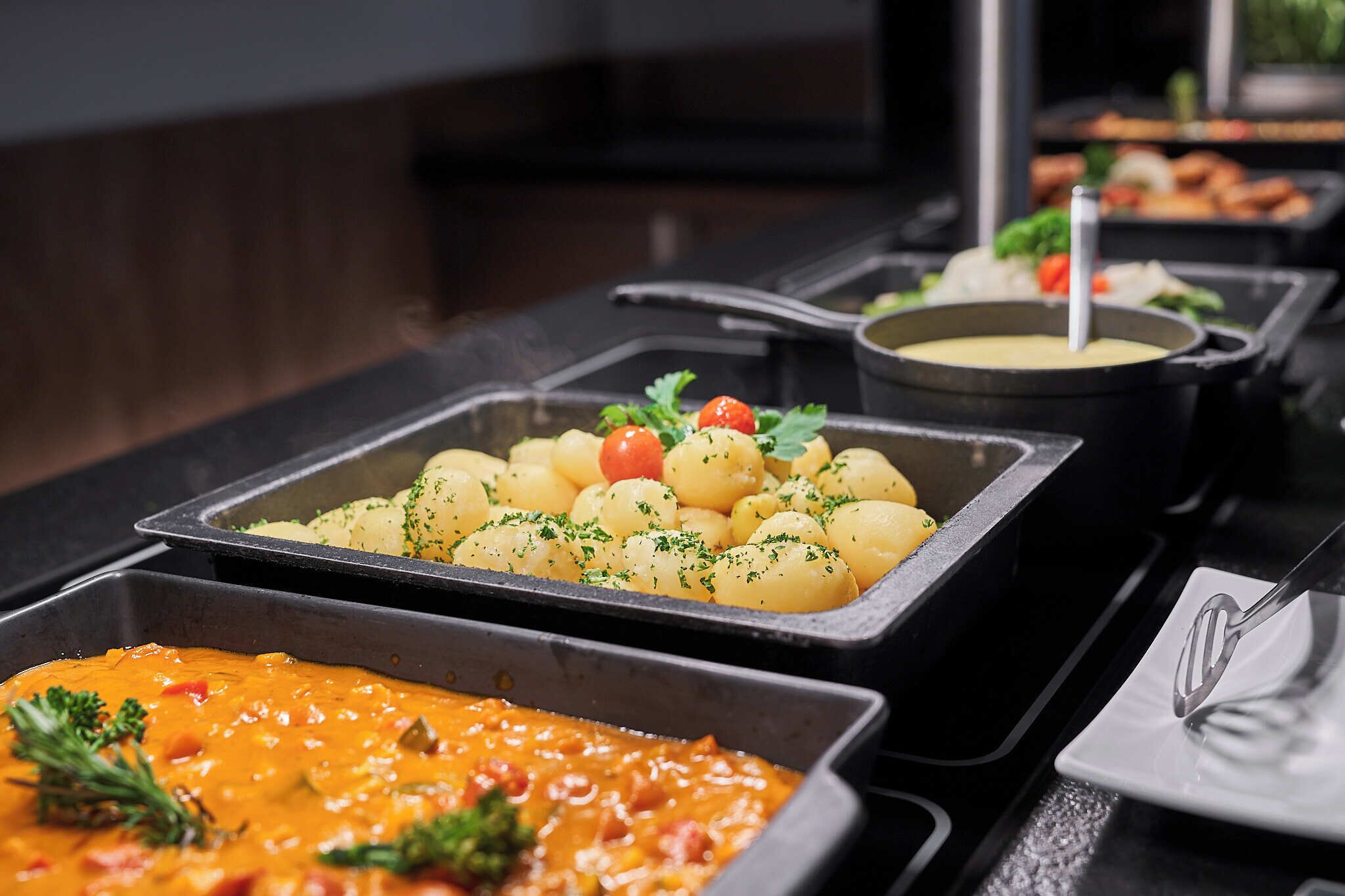 A buffet with various dishes including potatoes, a creamy sauce, and a soup.