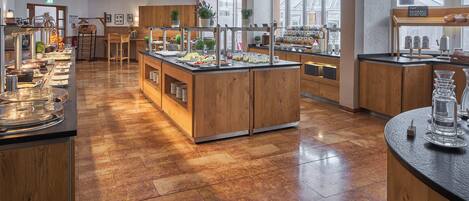 A spacious buffet area with multiple serving stations, wooden counters, and a variety of food and drink options.