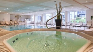An indoor swimming pool with clear water, surrounded by lounge chairs and a potted plant.