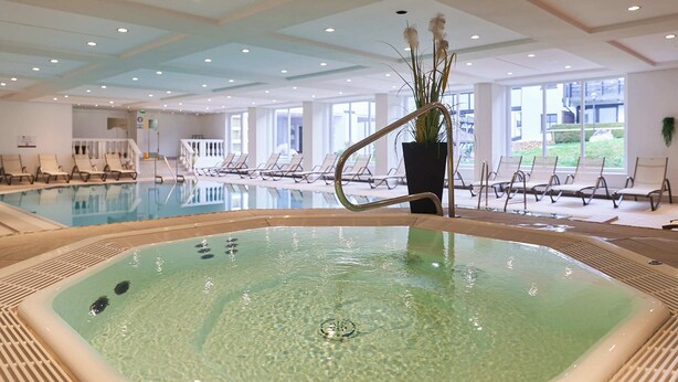 An indoor swimming pool with clear water, surrounded by lounge chairs and a potted plant. - Riessersee Hotel (Garmisch-Partenkirchen)