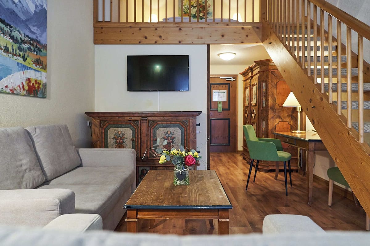 A living room with a wooden coffee table, a sofa, a TV mounted on the wall, and a staircase.