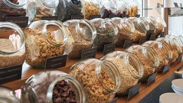 Diversos alimentos em potes de vidro com etiquetas, dispostos sobre um balcão de madeira.
