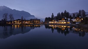 A lakeside hotel with multiple buildings reflecting on the water, surrounded by mountains.