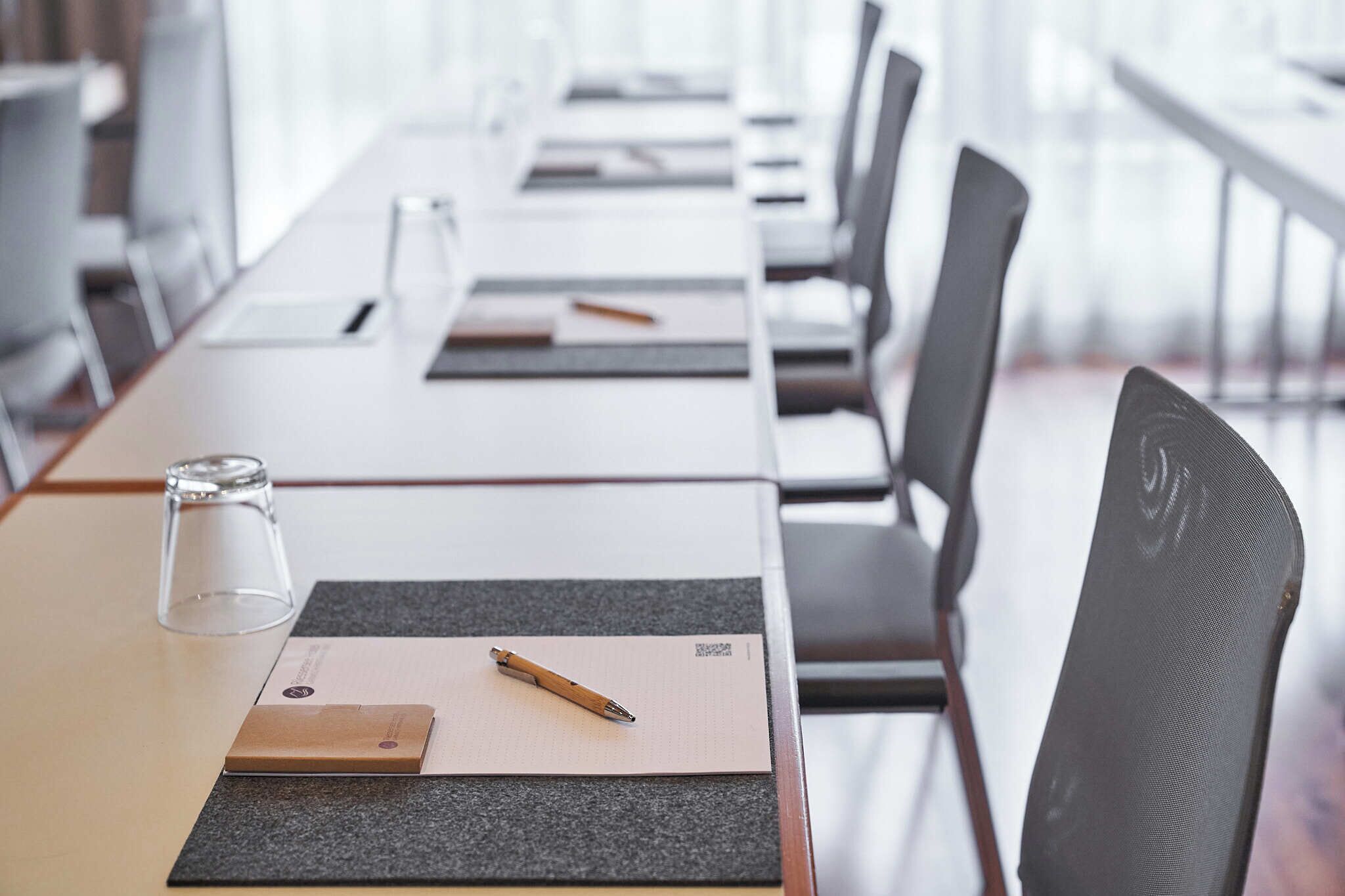 A conference room with a long table, chairs, a glass, a pen, and a notepad.