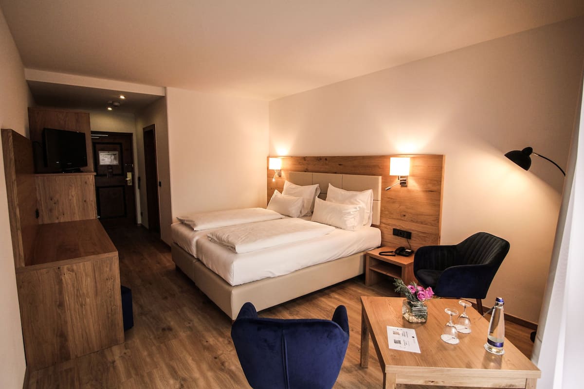 A hotel room with a bed, a desk, a chair, a TV, and a wooden cabinet.