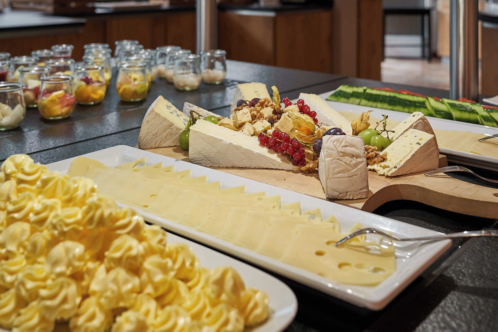 A buffet with various cheeses, fruits, and pastries.