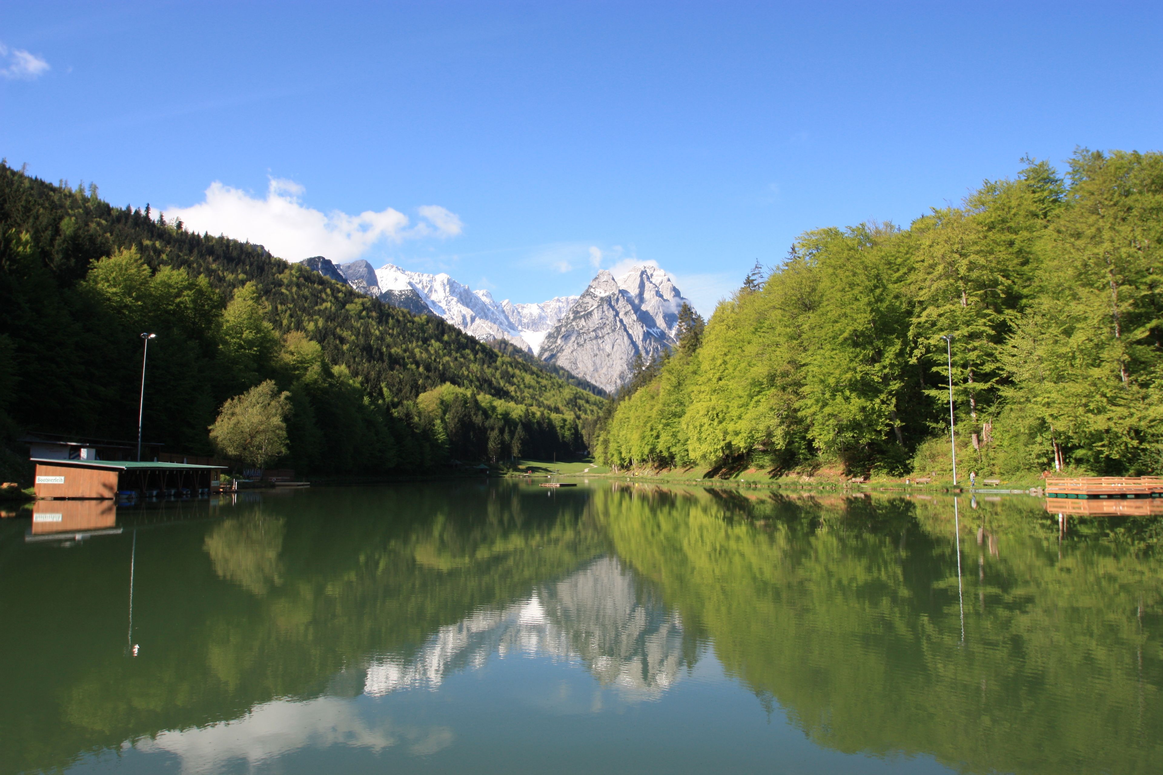 A calm lake with reflections of trees and mountains, surrounded by lush greenery and a wooden dock.