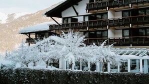 A multi-story building with balconies, a snow-covered roof, and a view of a mountainous landscape. - Riessersee Hotel (Garmisch-Partenkirchen)