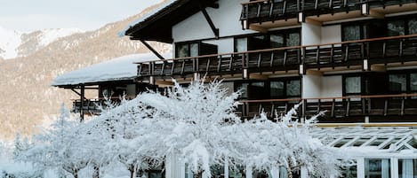 A multi-story building with balconies, a snow-covered roof, and a view of a mountainous landscape.