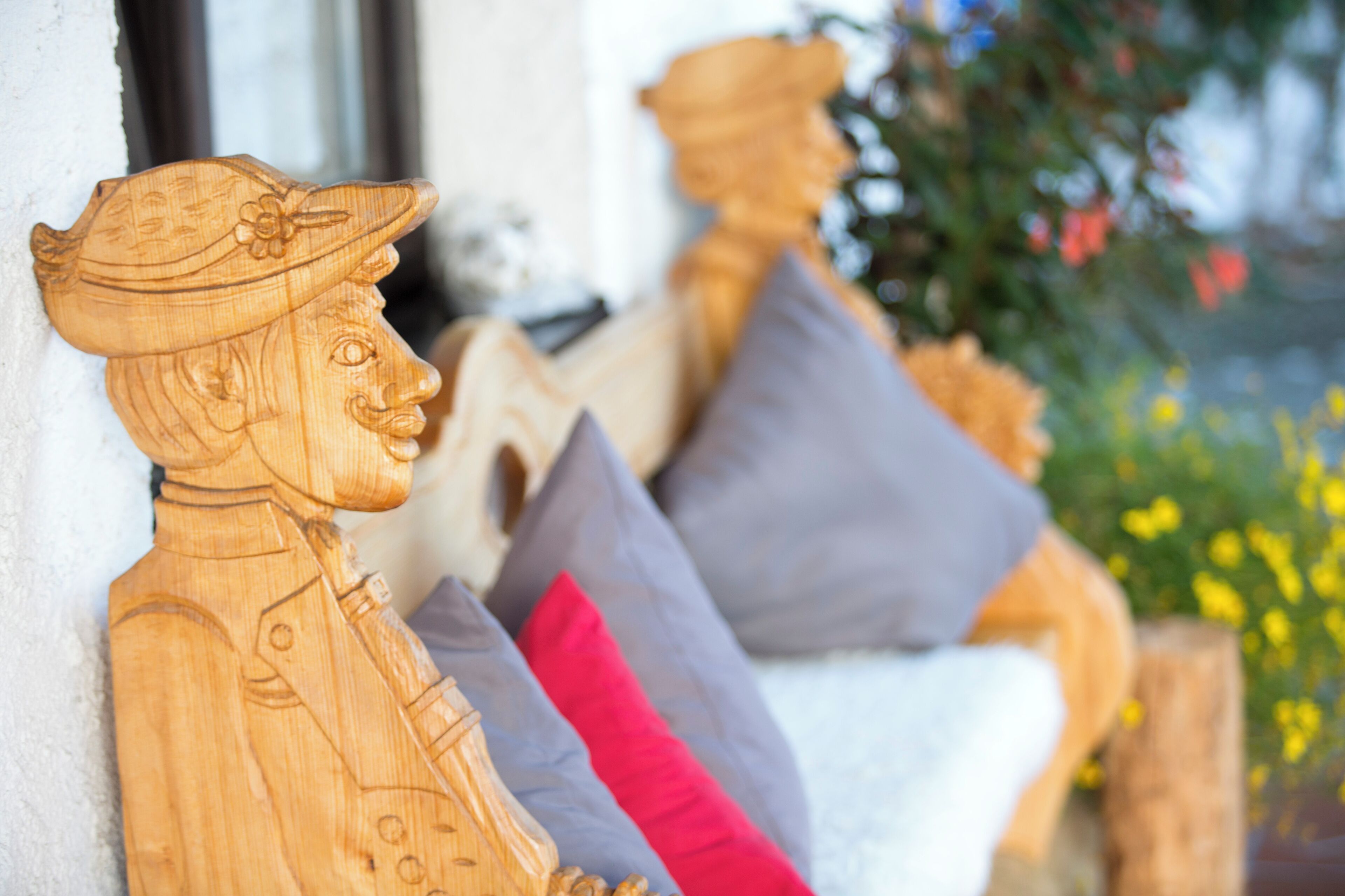 Wooden sculptures of a man and woman on a bench with cushions.
