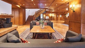 A spacious lobby with a wooden staircase, a central coffee table with a vase, and seating areas. - Riessersee Hotel (Garmisch-Partenkirchen)