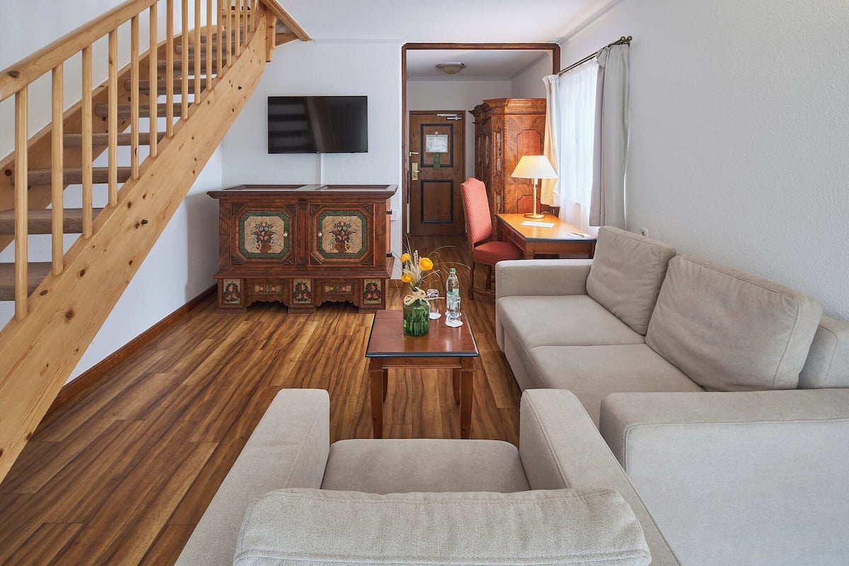 A living room with a wooden staircase, a sofa, a table with flowers, and a TV mounted on the wall.