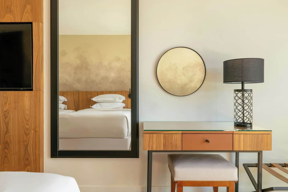 A hotel room with a bed, a desk with a lamp, and a large mirror.
