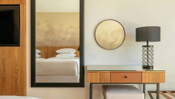 A hotel room with a bed, a desk with a lamp, and a large mirror.