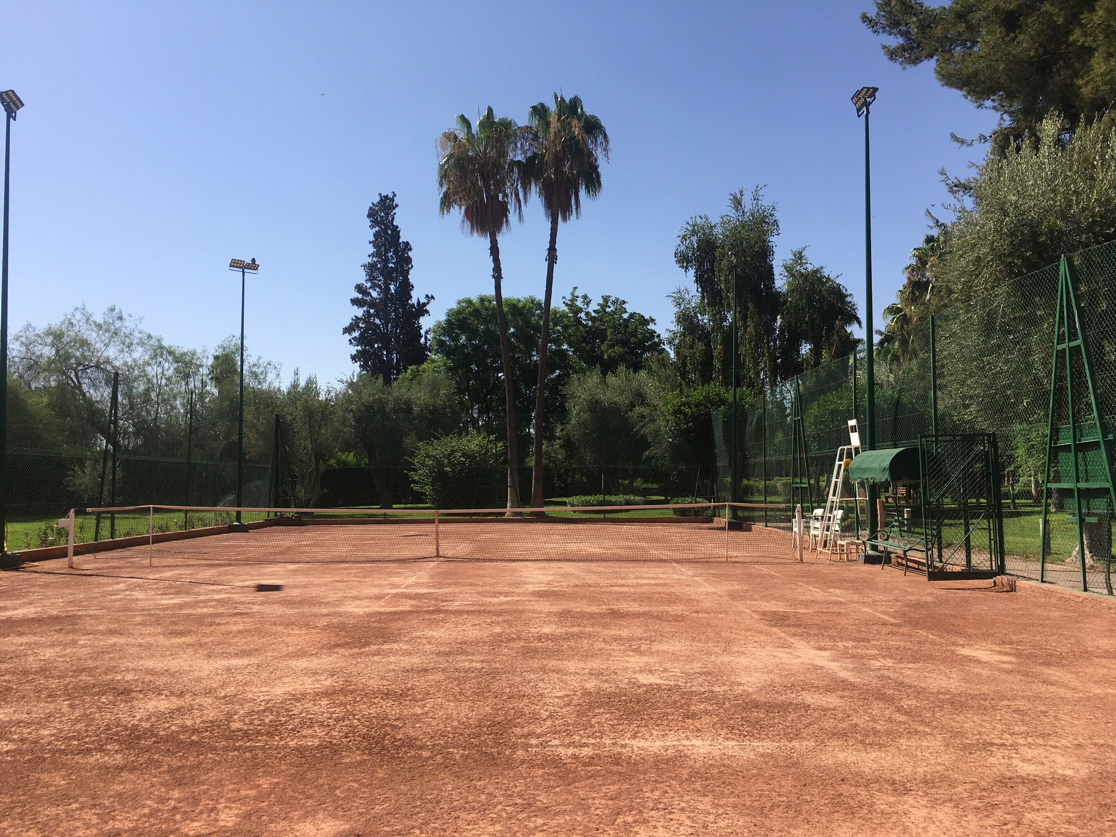 An outdoor tennis court with a net, surrounded by trees and a fence.