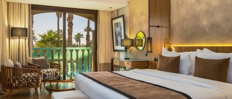 A hotel room with a large bed, a sitting area with a sofa and chairs, a balcony with a view of palm trees, and a wooden accent wall.