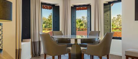 Un comedor moderno con una mesa redonda y seis sillas, ventanas amplias con cortinas y vistas al exterior con vegetación.