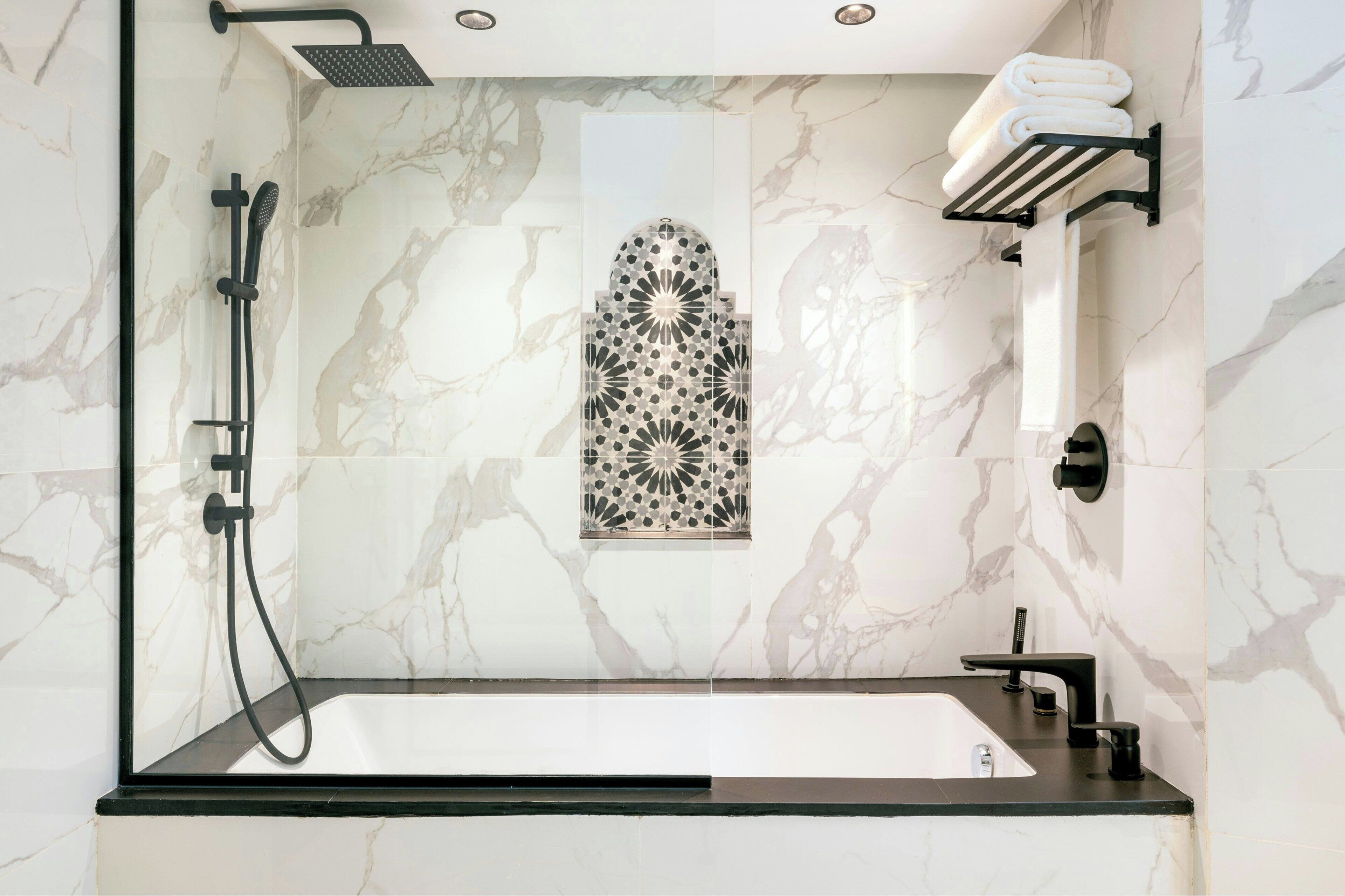A modern bathroom with a freestanding bathtub, a handheld showerhead, a towel rack, and a decorative tile wall.