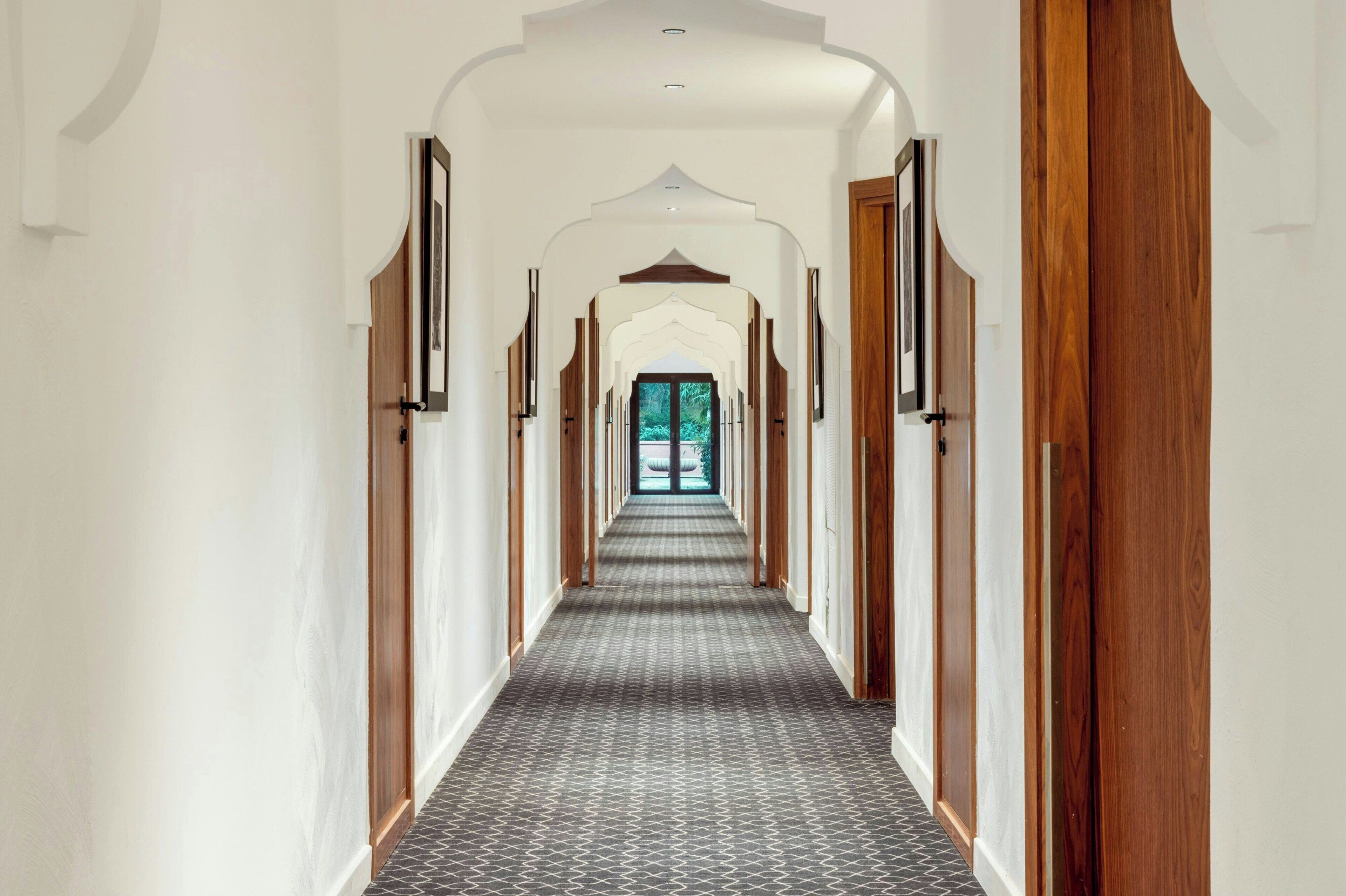 Un long couloir étroit, avec un revêtement de sol à motifs et des portes en bois de chaque côté.