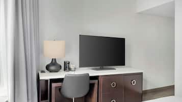 Habitación de hotel con escritorio, silla, televisor, lámpara y cama.