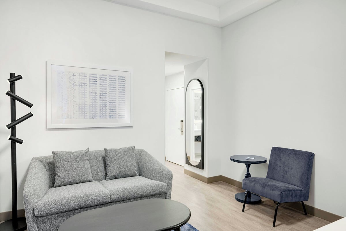 A modern room with a grey sofa, a round table, a blue armchair, a black floor lamp, and a framed list on the wall.
