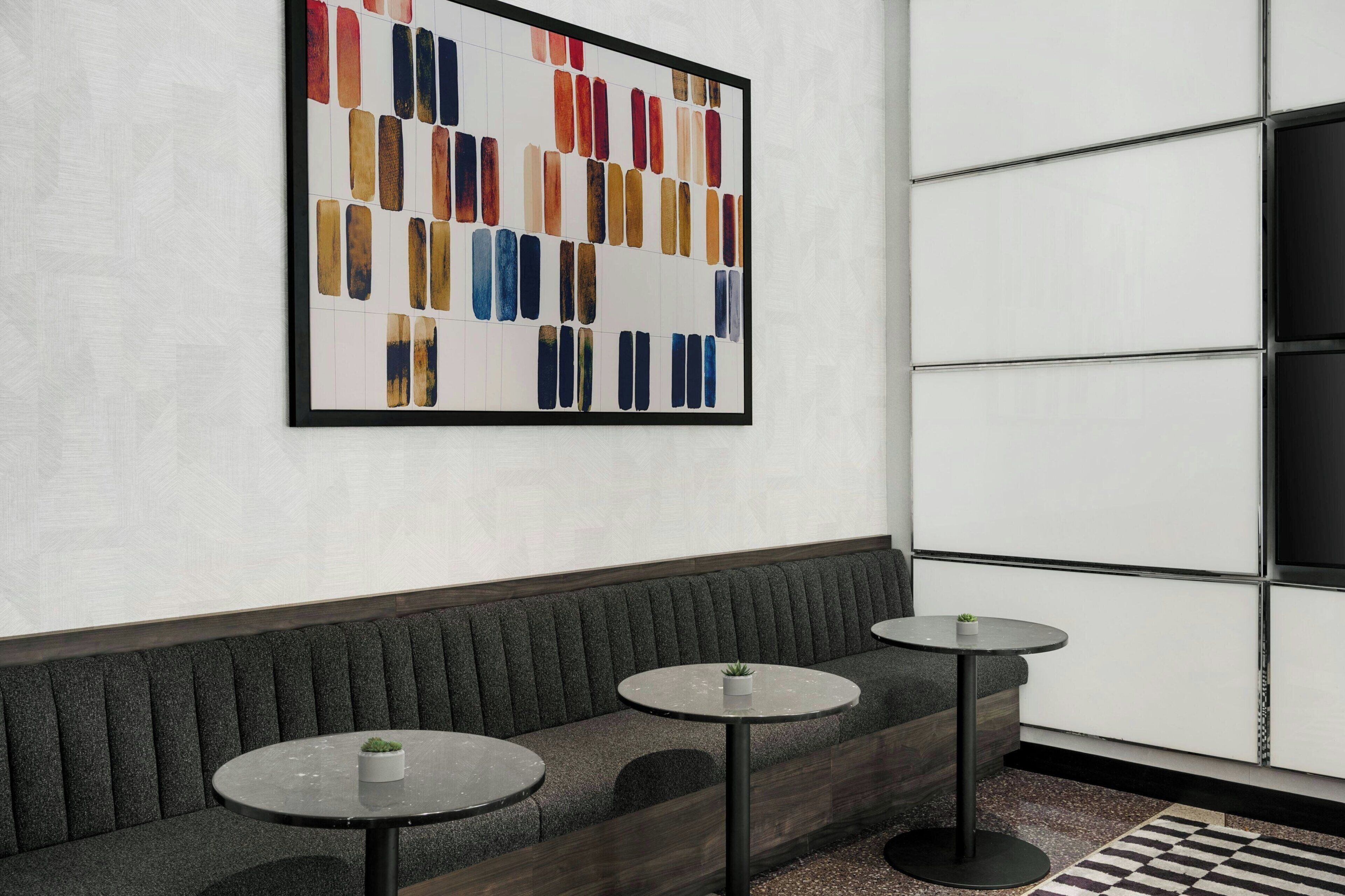 Un intérieur moderne avec un canapé, deux tables rondes et un grand tableau abstrait accroché au mur.