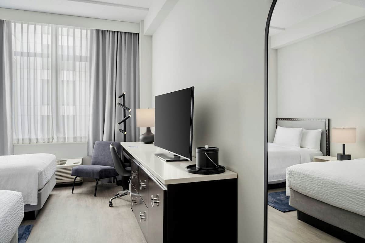 A hotel room with two beds, a desk with a computer, a chair, a TV, and a large mirror.