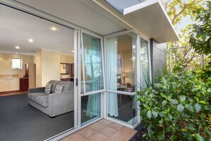 A modern living area with a grey sofa, a glass sliding door, and a view of a kitchen and dining area. - Aristotles North Shore (Auckland)