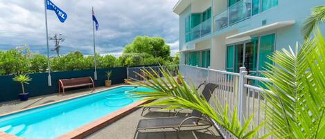 A swimming pool with lounge chairs, a bench, and a flag.