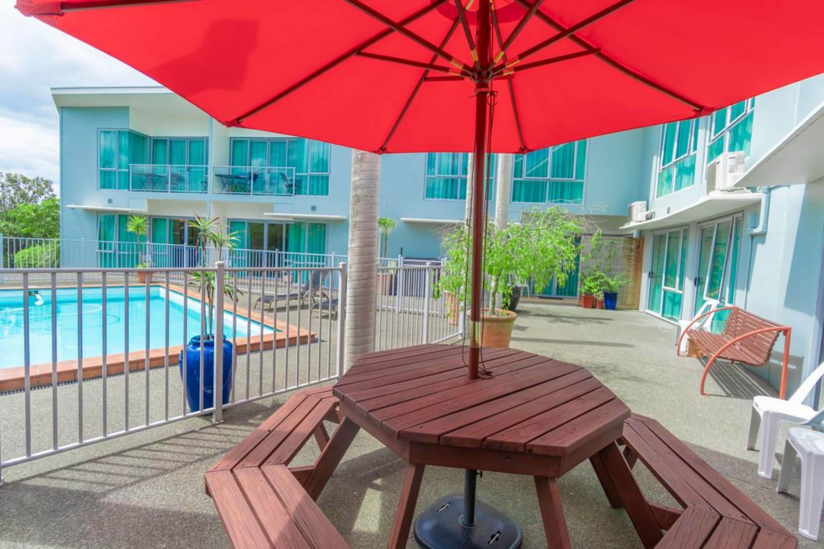 A poolside area with a wooden table and bench, surrounded by a metal fence.
