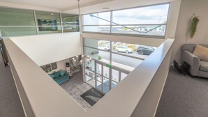 A modern hotel lobby with a high ceiling, large windows, a seating area with a sofa, and a view of the street outside. - Aristotles North Shore (Auckland)