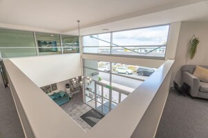 A modern hotel lobby with a high ceiling, large windows, a seating area with a sofa, and a view of the street outside.