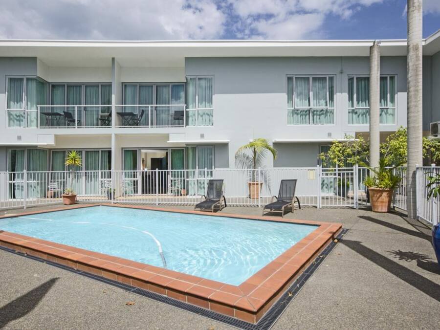 Un hotel moderno con piscina en la azotea, varios balcones y zonas de estar al aire libre.