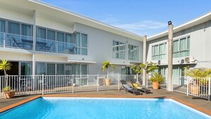 A modern hotel with a swimming pool, outdoor seating, and a white fence. - Aristotles North Shore (Auckland)