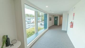 A hallway with large windows, a small table with a plant, and a fire extinguisher on the wall.