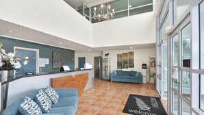 A reception area with a reception desk, a blue sofa with patterned cushions, a 'welcome' mat, and a chandelier. - Aristotles North Shore (Auckland)