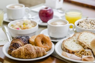 Una colazione con croissant, ciambelle, pane, formaggio e una ciotola di frutta.