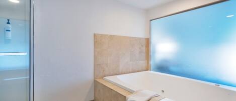 Un baño moderno con bañera, cabina de ducha de vidrio y un espejo grande.