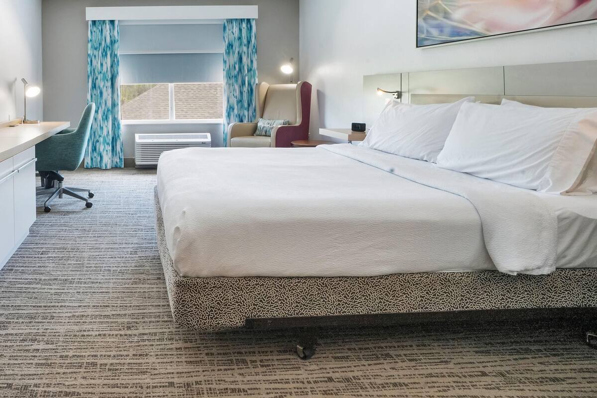 Una camera d'albergo con un letto, una scrivania, una sedia e una finestra con tende.