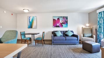 Une chambre d’hôtel comprenant une table à manger, deux chaises, un canapé avec des coussins, un lampadaire et des œuvres d’art abstraites accrochées au mur.
