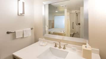 A bathroom with a white sink, two faucets, a mirror, a towel rack with two towels, and a soap dispenser.