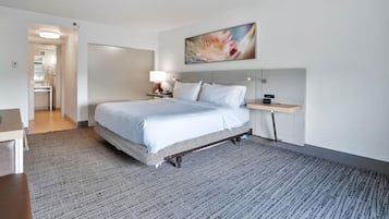 Una habitación de hotel con cama, mesita de noche, lámpara y un cuadro en la pared.
