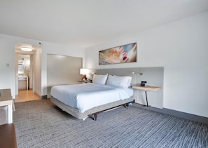 A hotel room with a bed, bedside table, lamp, and a painting on the wall. - Hilton Garden Inn Jacksonville Airport (Jacksonville)