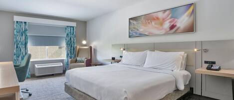 A hotel room with a large bed, a desk, a chair, a window with curtains, and a painting on the wall.