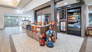 Un área comercial moderna con mostrador, dispensadores de aperitivos y vitrinas refrigeradas para bebidas.