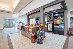 A modern retail area with a counter, snack dispensers, and refrigerated beverage displays. - Hilton Garden Inn Jacksonville Airport (Jacksonville)