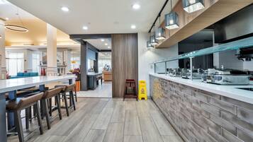 Une cuisine moderne avec un mur recouvert de briques, des appareils électroménagers en acier inoxydable et un coin bar avec des tabourets.