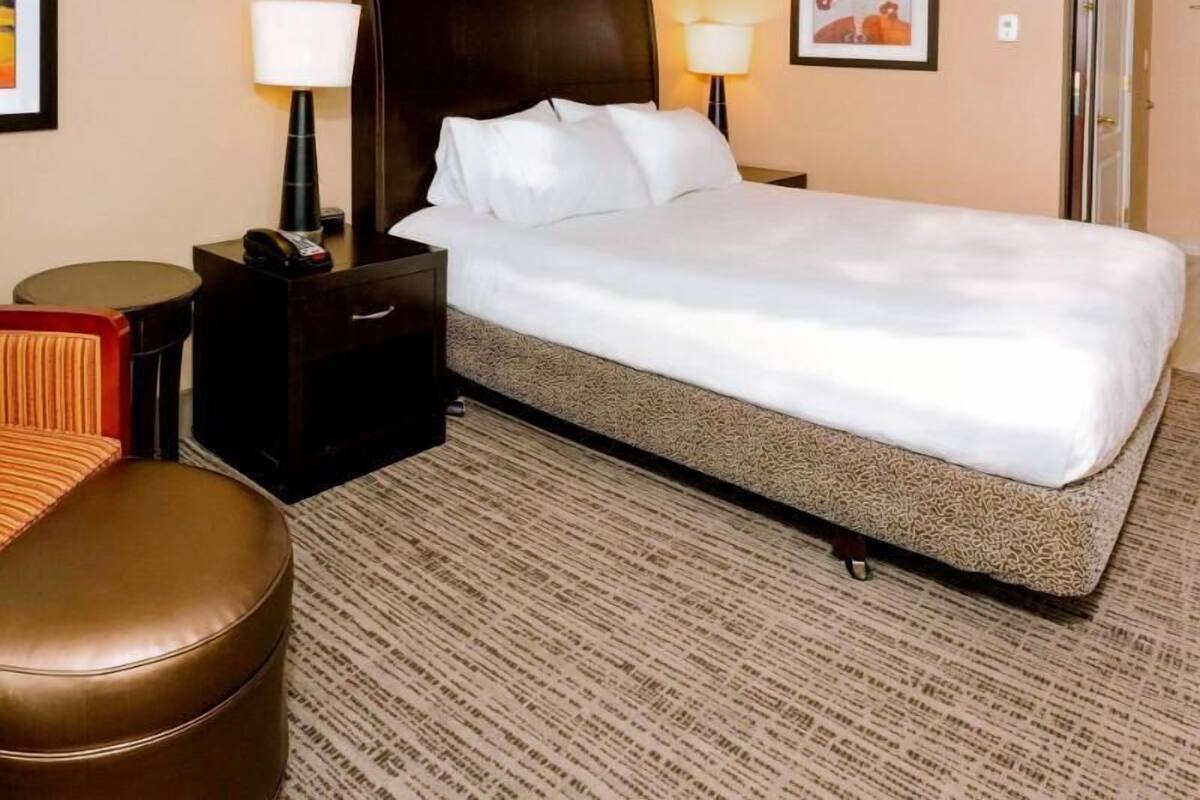 Una camera d'albergo con un letto, comodini, una lampada, una sedia e un pavimento rivestito di moquette.