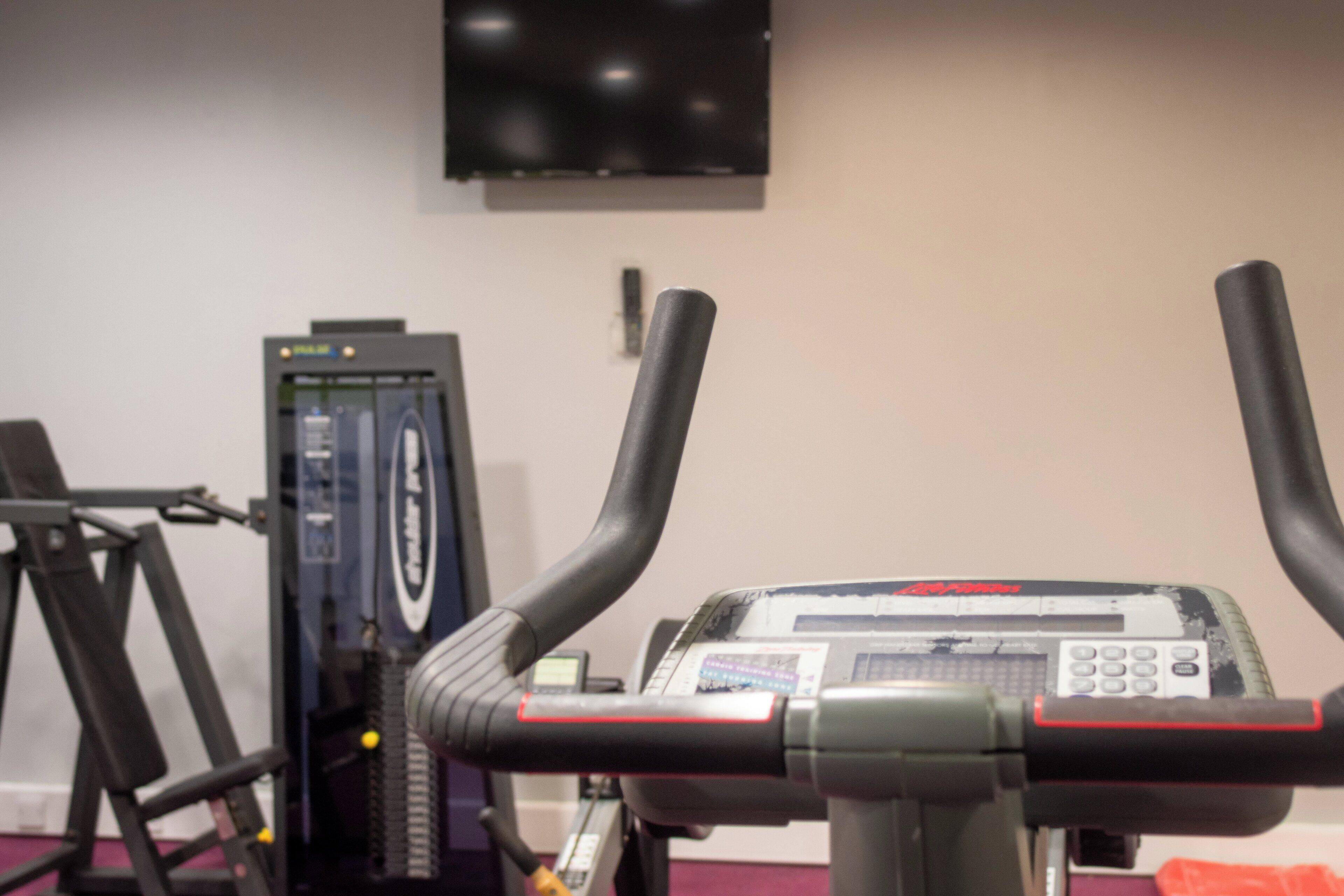 A stationary bike with a digital display, a television mounted on the wall, and a weight machine in the background.