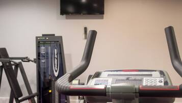 A stationary bike with a digital display, a television mounted on the wall, and a weight machine in the background.